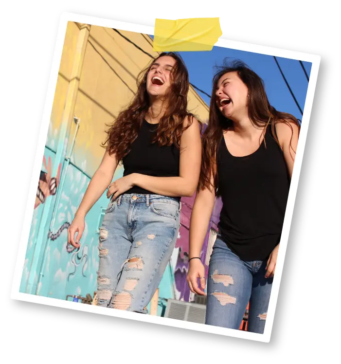 Two young women laugh together as they walk in front of a graffitied wall